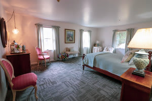 A cozy bedroom with a large bed, carpeted floor, and classic decor.