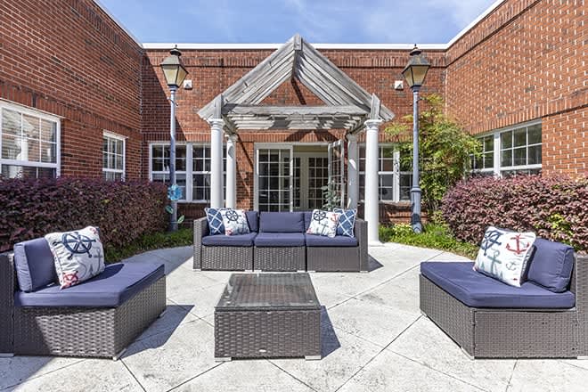 A cozy outdoor seating area with wicker furniture in a courtyard bordered by a brick building.