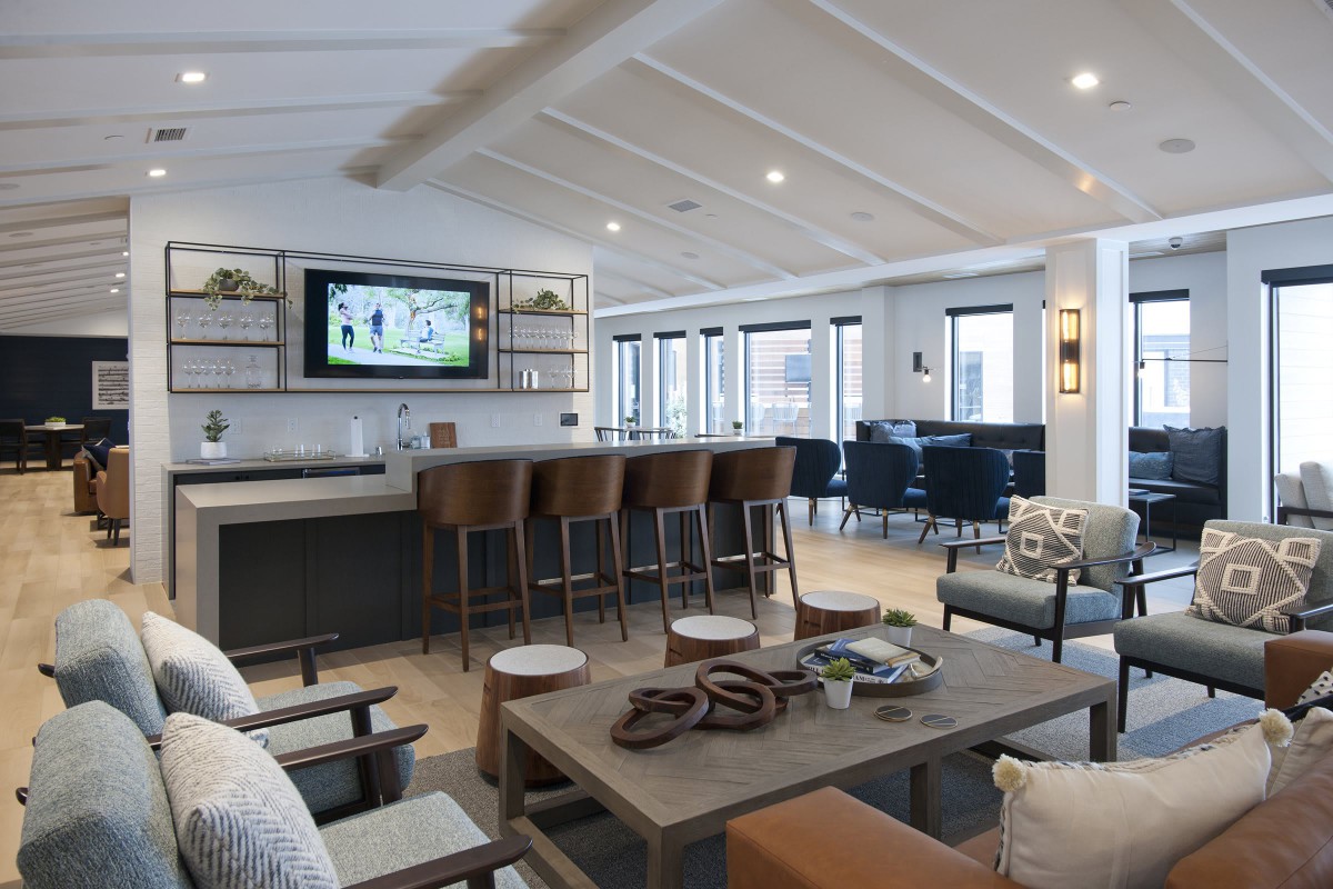 A modern living room with an open bar area and comfortable seating, featuring a television and stylish wooden furniture.