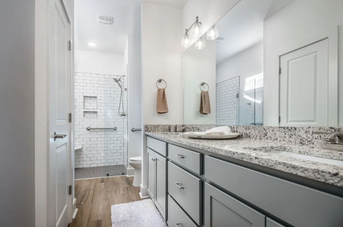 A modern bathroom with a large mirror, granite countertop, and a walk-in shower.