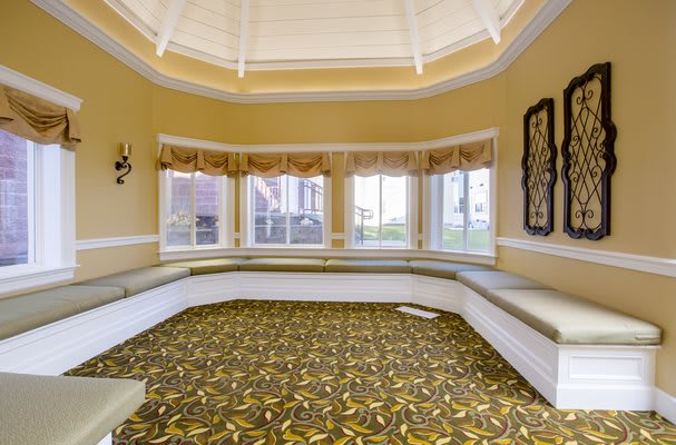 An empty room with a patterned carpet and built-in seating beneath large windows.