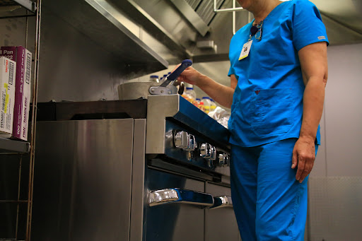 A healthcare worker in blue scrubs prepares food in a kitchen setting.