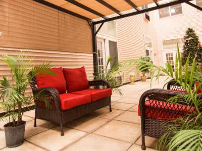 A cozy outdoor patio with red-cushioned wicker furniture and a pergola.