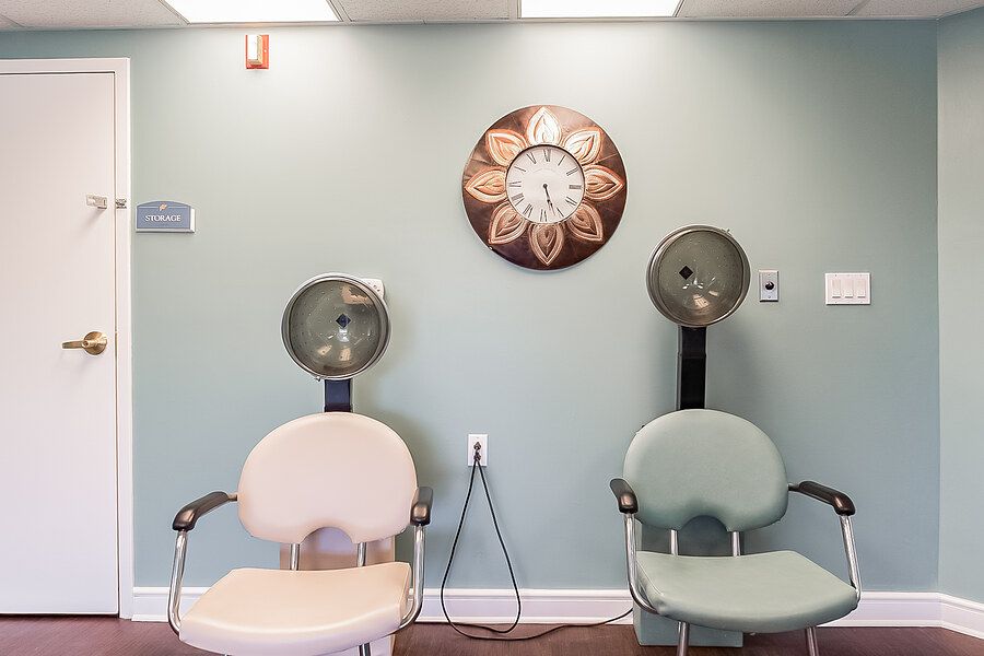 A salon waiting area featuring two hair drying chairs and a decorative wall clock.