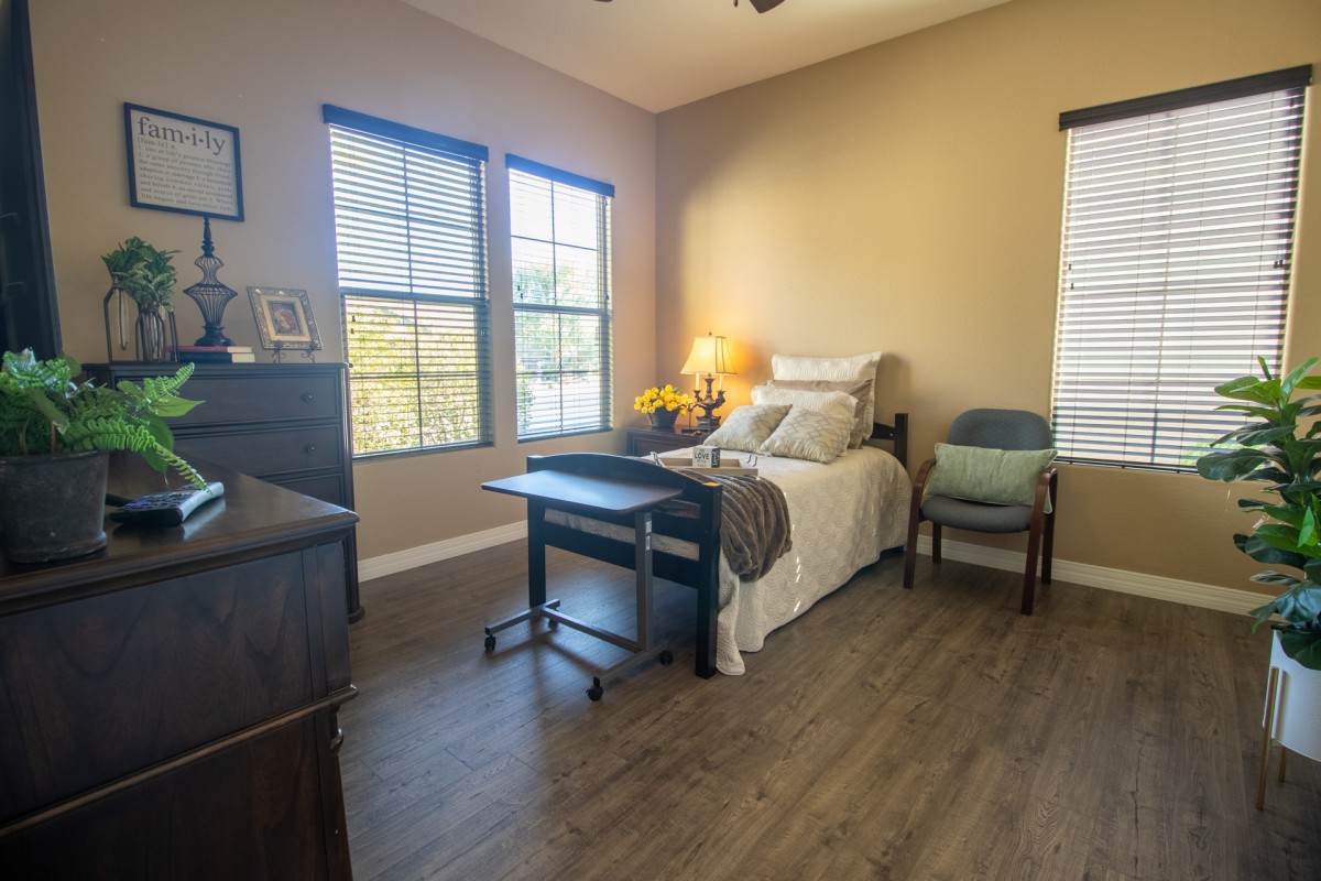 A cozy bedroom with a single bed, lamp, and large windows letting in sunlight.