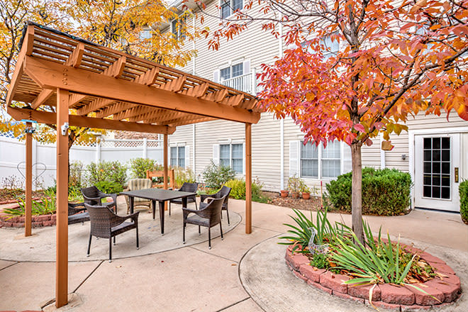 A cozy patio with a pergola and outdoor seating, surrounded by autumn foliage.