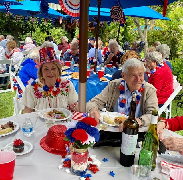 A festive outdoor gathering with patriotic decorations and attendees enjoying food and drinks.