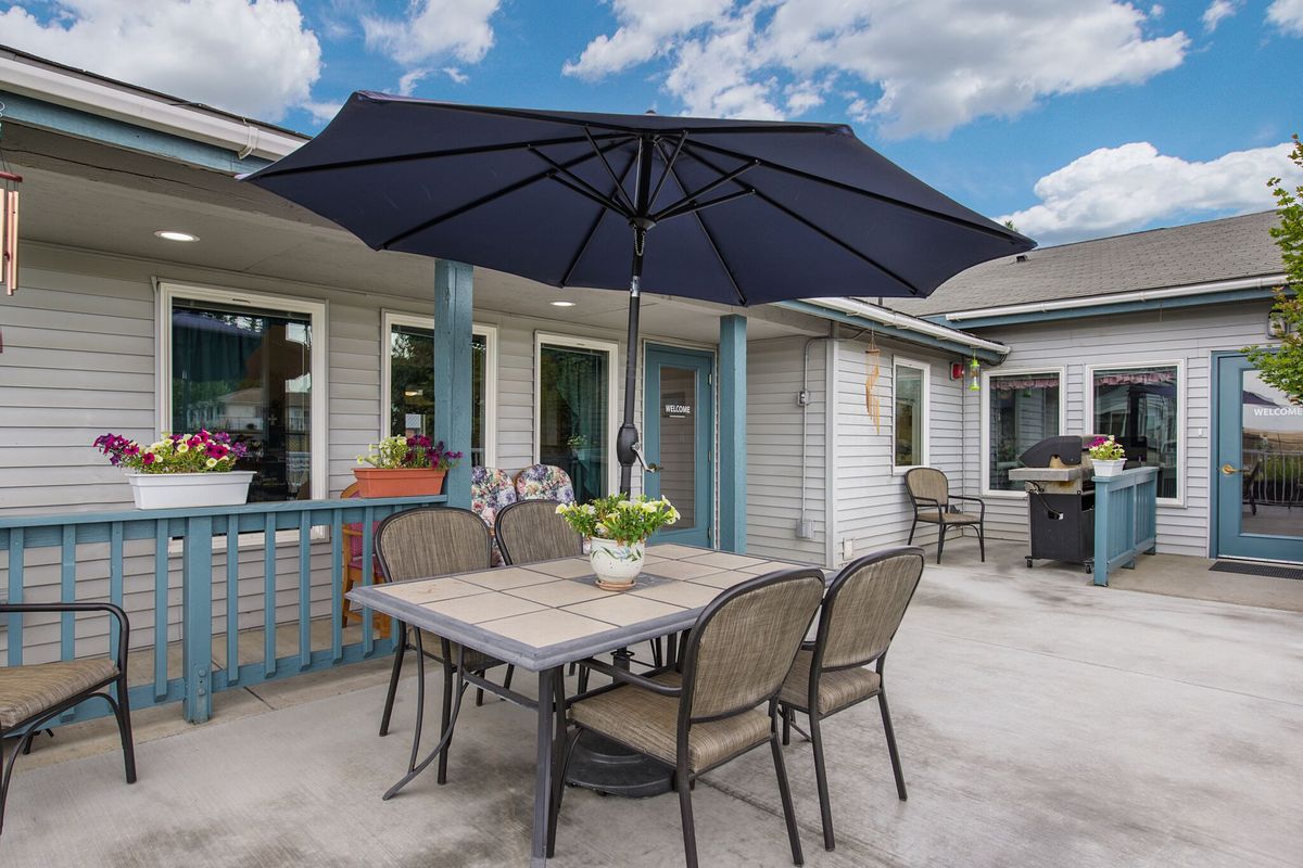 A cozy outdoor patio setup with a table, chairs, and a large umbrella under a partly cloudy sky.