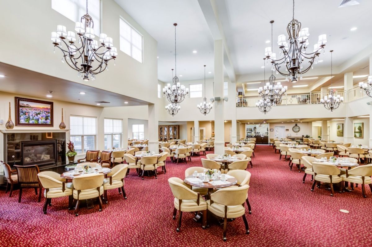 A spacious dining area with elegant chandeliers and neatly arranged tables and chairs on a red carpet.