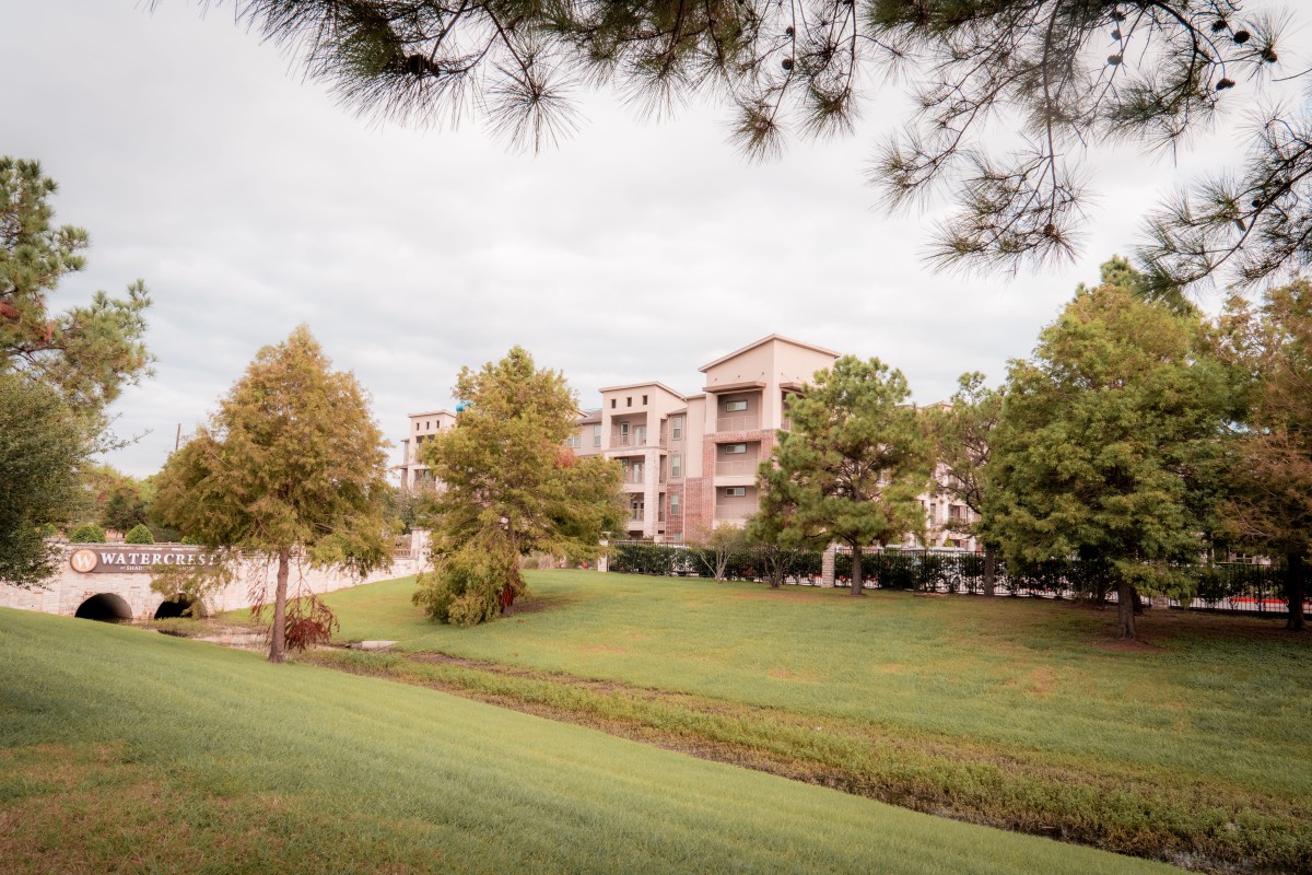 A scenic view of apartment buildings surrounded by lush greenery and trees under a cloudy sky.