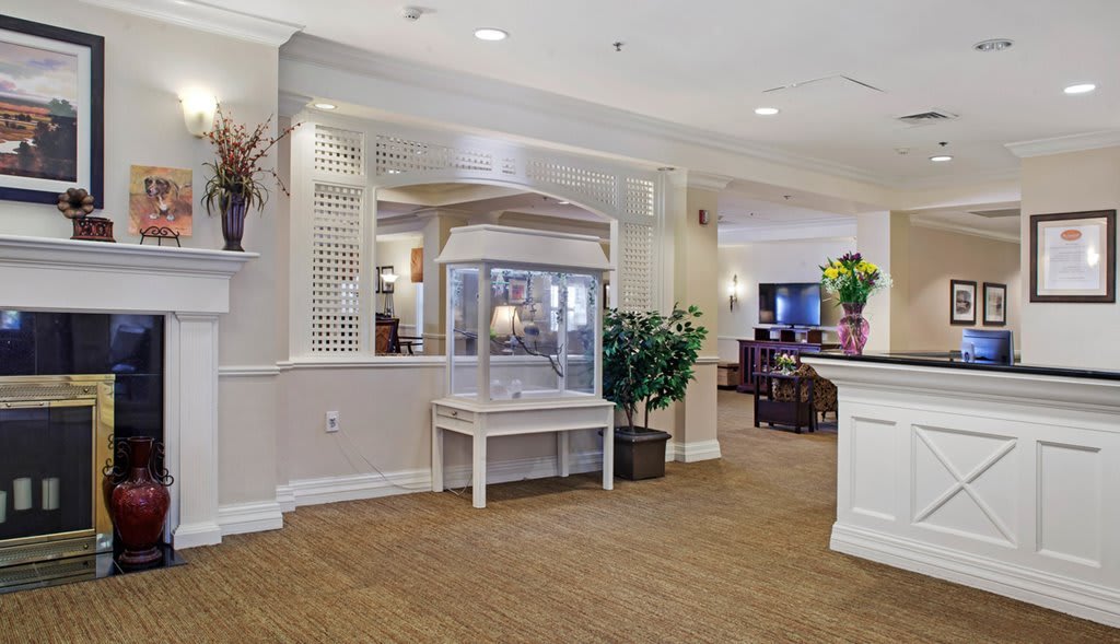 A hotel lobby with a popcorn machine, seating area, and reception desk surrounded by plants and flowers.