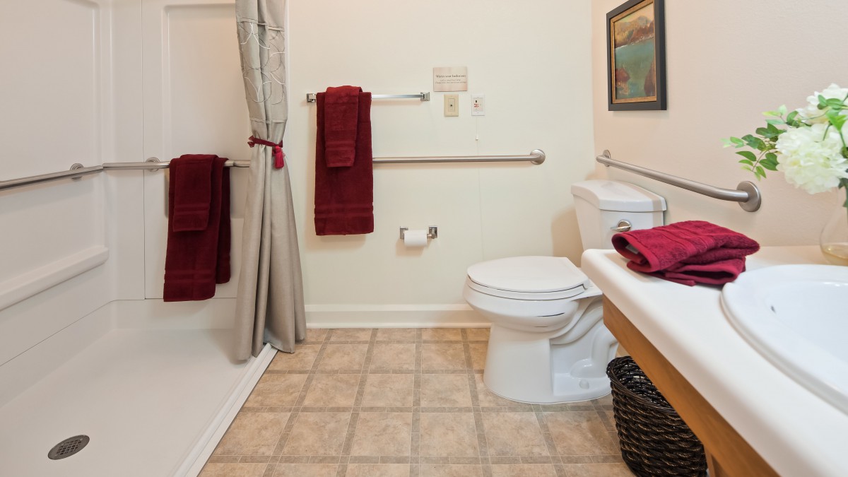 A clean and simple bathroom featuring a toilet, shower, and red towel accents.