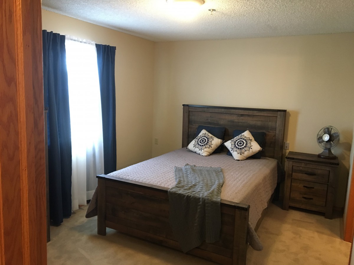 A cozy bedroom with a wooden bed frame, two decorative pillows, and dark blue curtains.