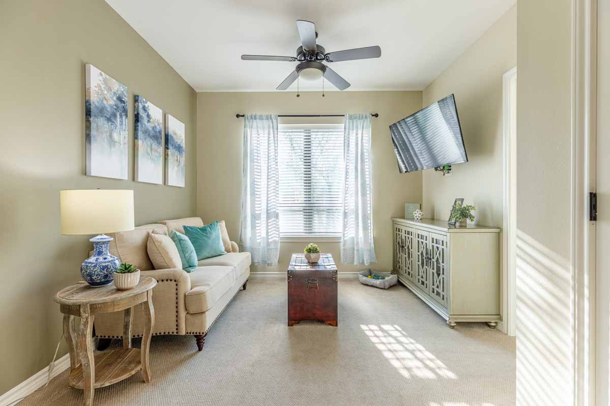 A cozy living room featuring a beige sofa, ceiling fan, and mounted television with elegant decor and ample natural light.