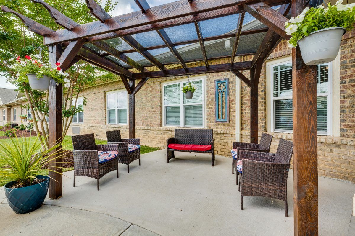 A cozy outdoor patio with rattan furniture set under a pergola, adjacent to a brick building.