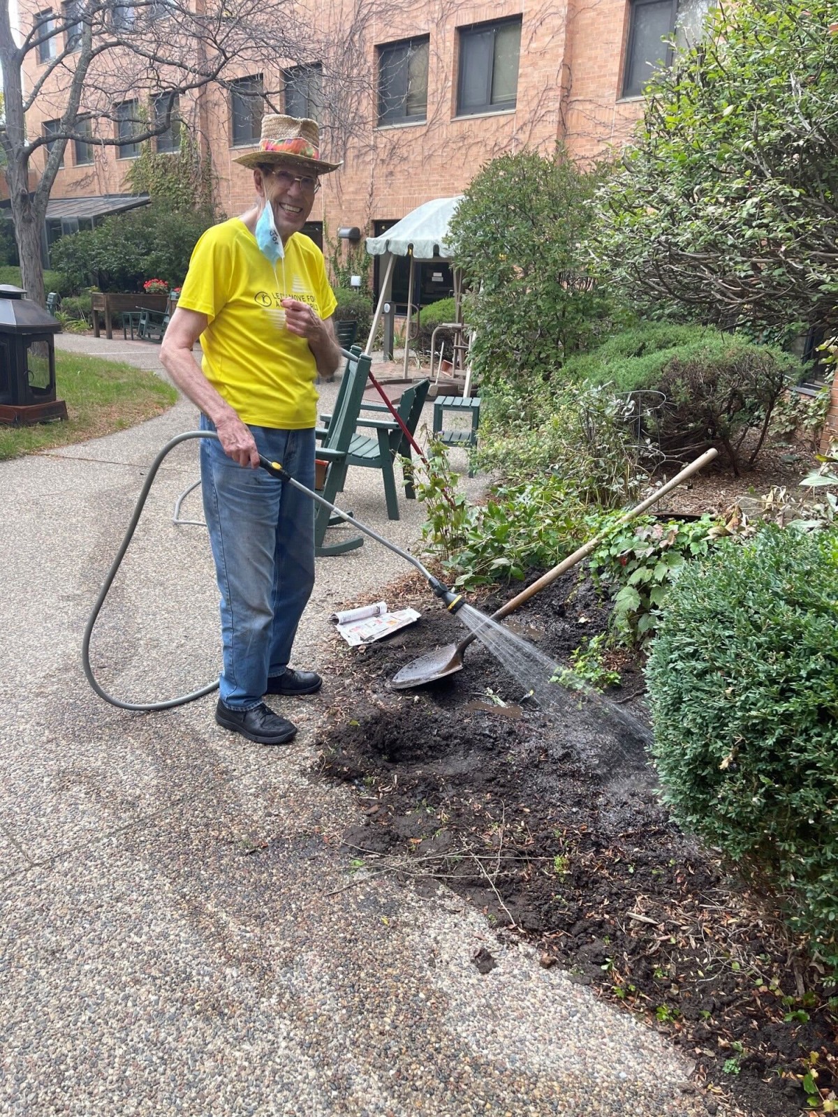 Person watering plants in a garden setting, wearing a yellow shirt and hat.