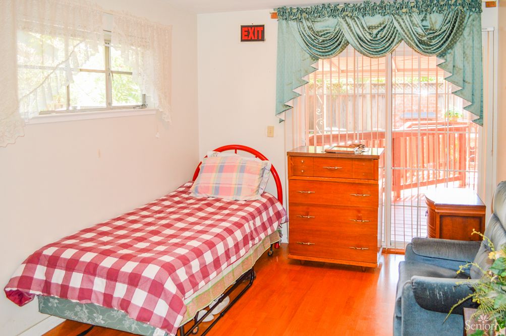 A cozy bedroom with a single bed and plaid bedding, featuring a window, chest of drawers, and hardwood flooring.