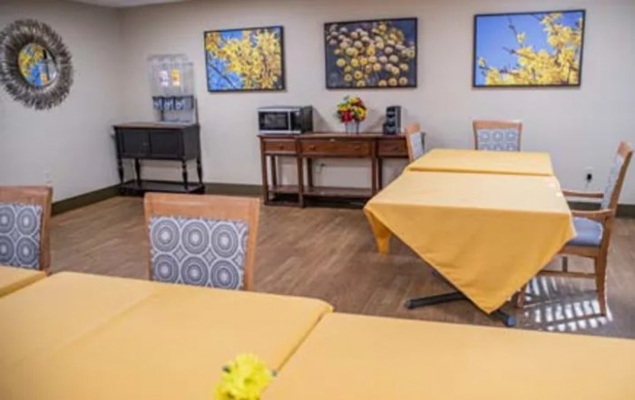 A dining room with yellow tablecloths and floral wall art.