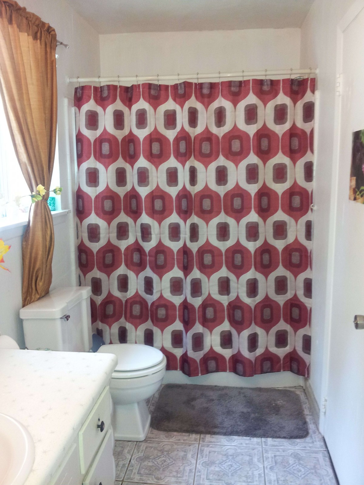A bathroom featuring a red and white patterned shower curtain, with a toilet and sink visible.