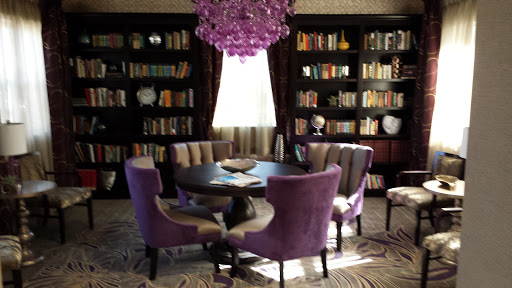 A stylish dining area featuring purple chairs and a modern chandelier, surrounded by bookshelves filled with books.