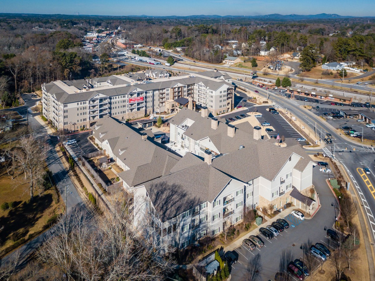 Aerial view of a residential community with buildings, roads, and parking lots surrounded by trees.