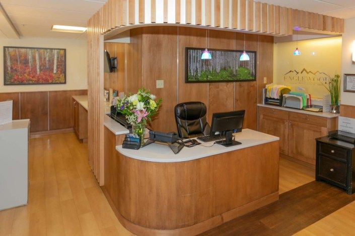 A modern reception area with a wooden desk, computer, and decorative flowers.