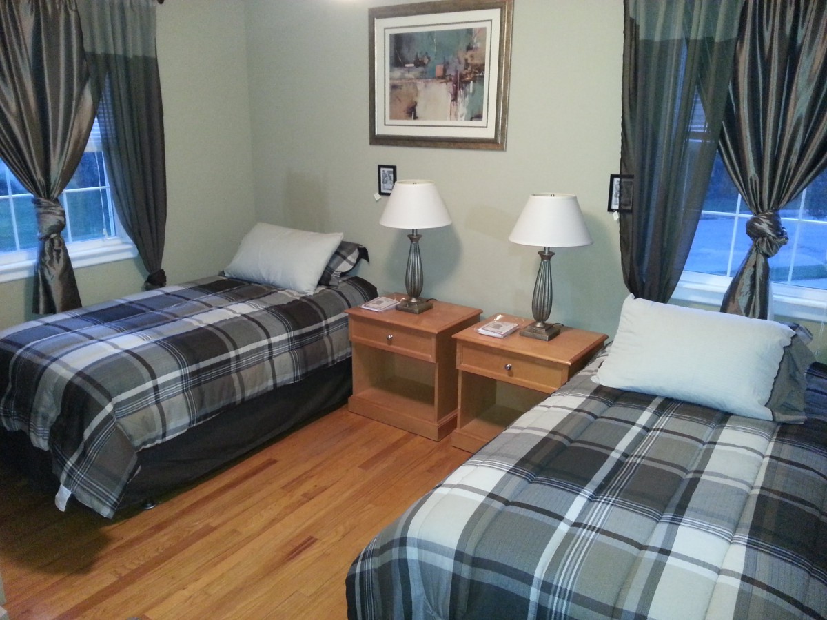 A neatly arranged bedroom with twin beds featuring plaid bedding, two lamps on wooden nightstands, and elegant curtains.