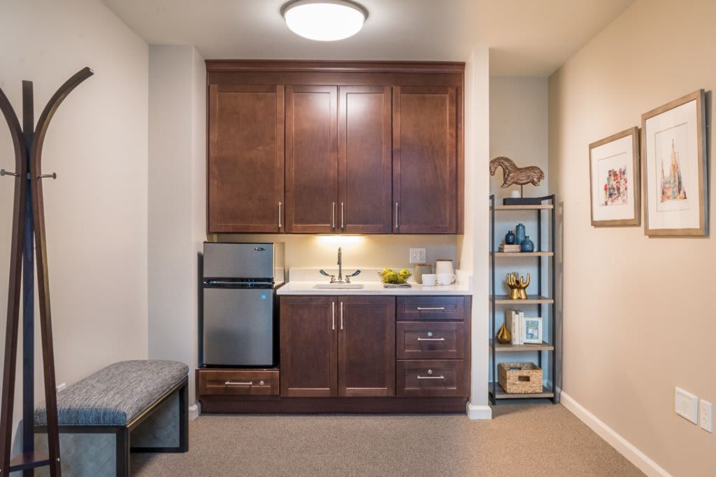 A compact kitchenette featuring wooden cabinets, a small fridge, and a neatly organized shelving unit.