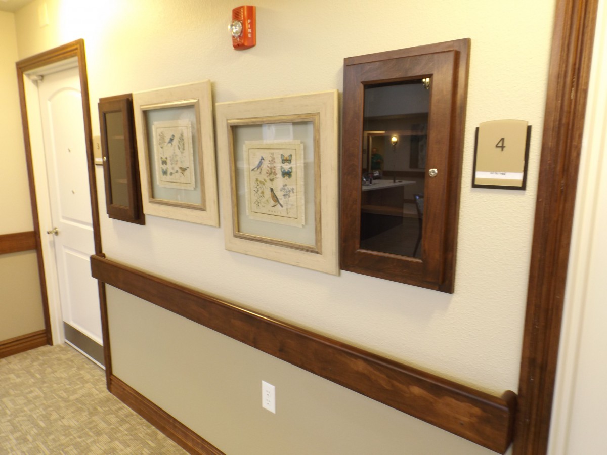 A hallway with framed artwork and a display case mounted on the wall.