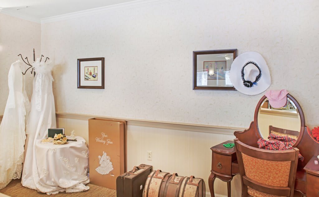 A cozy interior room featuring framed artwork, a small table with decor items, and vintage suitcases leaning against the wall.