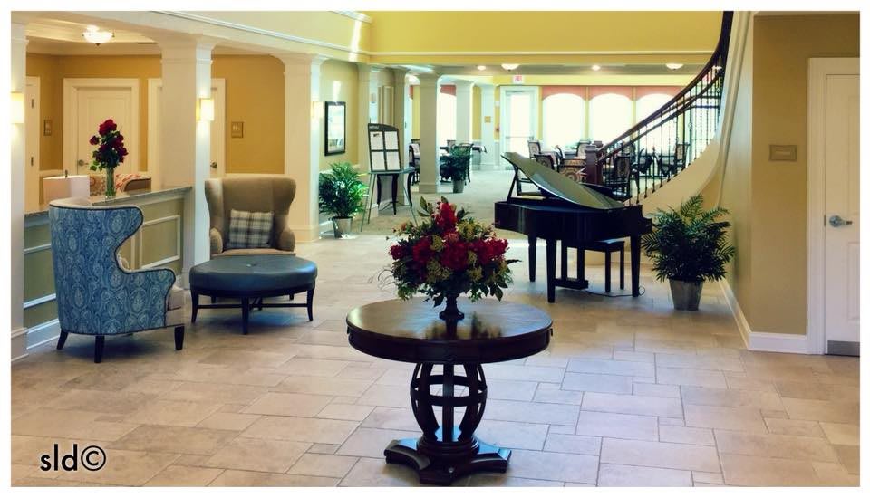 A spacious and elegant lobby featuring a grand piano, round table with floral arrangement, and comfortable seating.