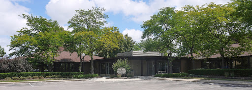 A modern building surrounded by lush greenery and a clear, partly cloudy sky.