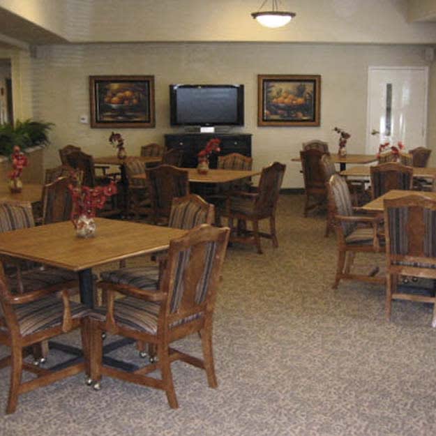 A cozy indoor dining area with wooden tables and chairs, decorated with paintings and a television on the wall.