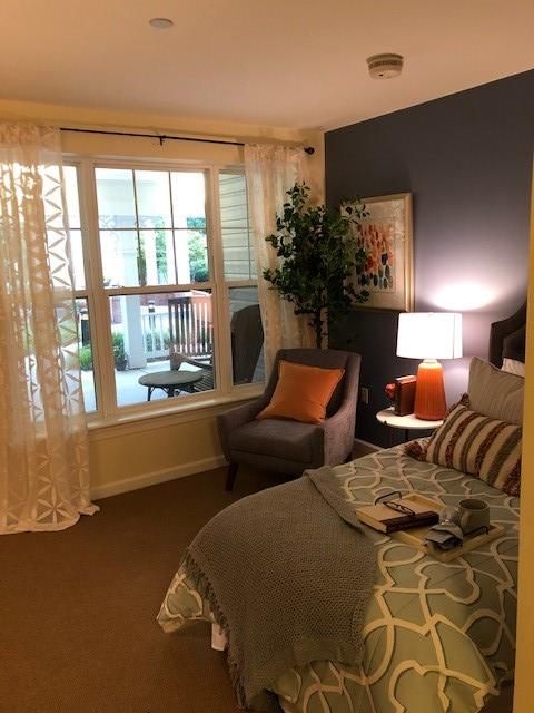 A cozy bedroom with warm lighting, featuring an armchair by a large window and stylish decor.