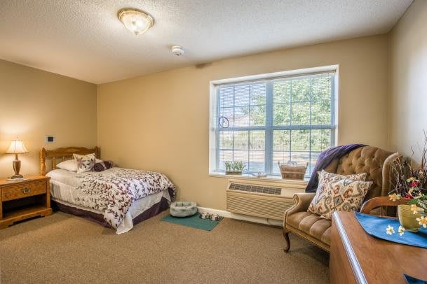 A cozy bedroom with a single bed, chair, and large window offering natural light.