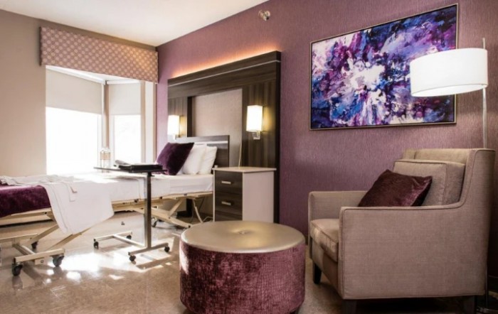 A modern hospital room with elegant interior design, featuring a comfortable chair, a hospital bed, and abstract artwork on the wall.