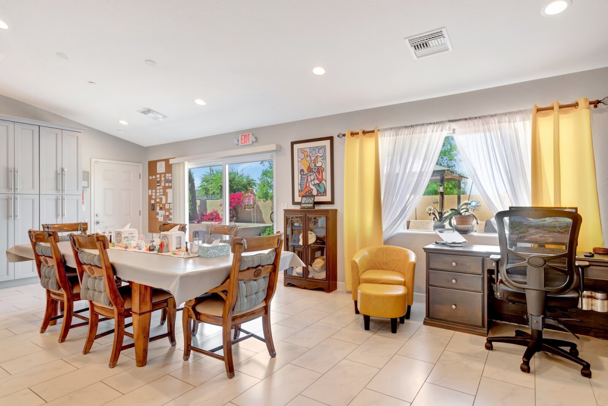 A cozy dining and office area with wooden furniture and decorative elements, featuring a window with a garden view.