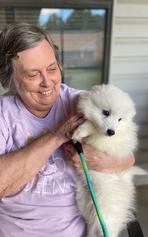 A smiling woman holding a fluffy white puppy outside.