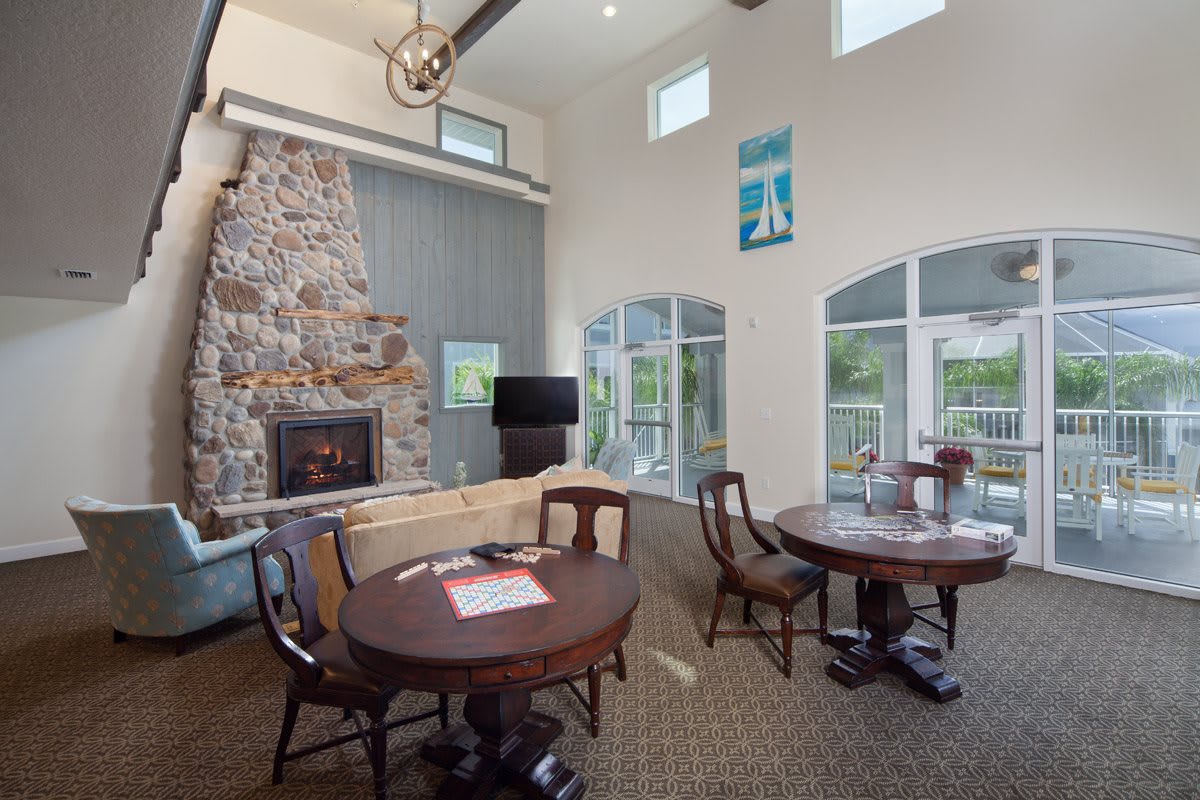 A cozy living room with a stone fireplace, tables, and chairs near large windows.