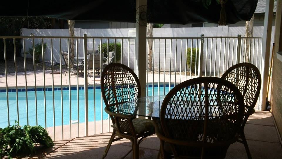 Outdoor patio area with chairs overlooking a fenced pool on a sunny day.