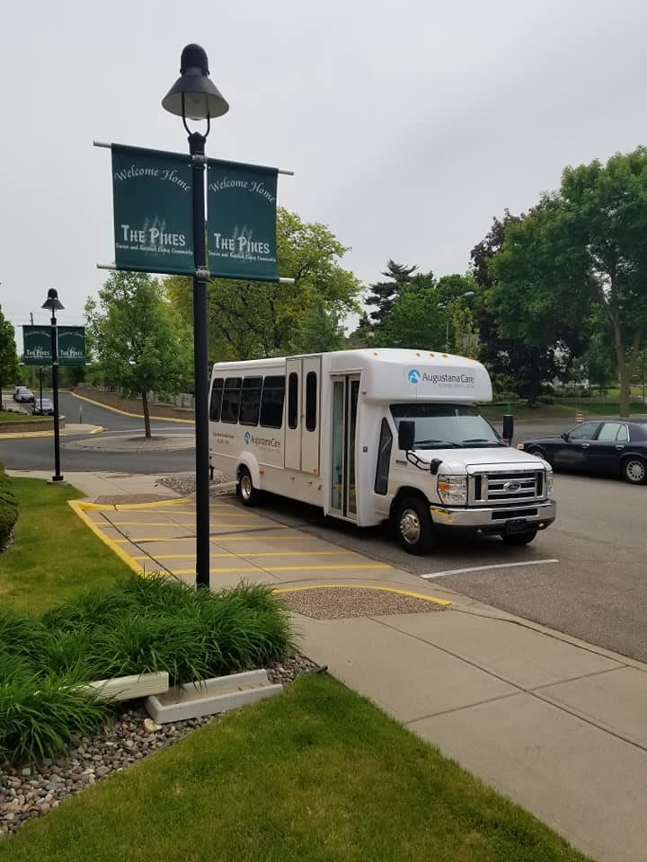 A shuttle bus parked in a lot near green trees and signage on an overcast day.
