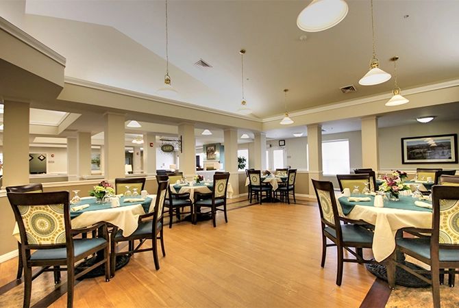 A well-lit dining area with neatly arranged tables and chairs on a wooden floor.
