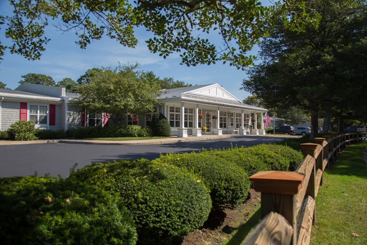 A charming building surrounded by well-maintained bushes and trees, with a clear driveway in front.