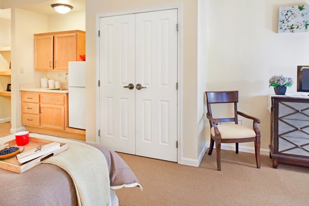 A cozy bedroom with a view of the kitchen, featuring a chair and double doors.