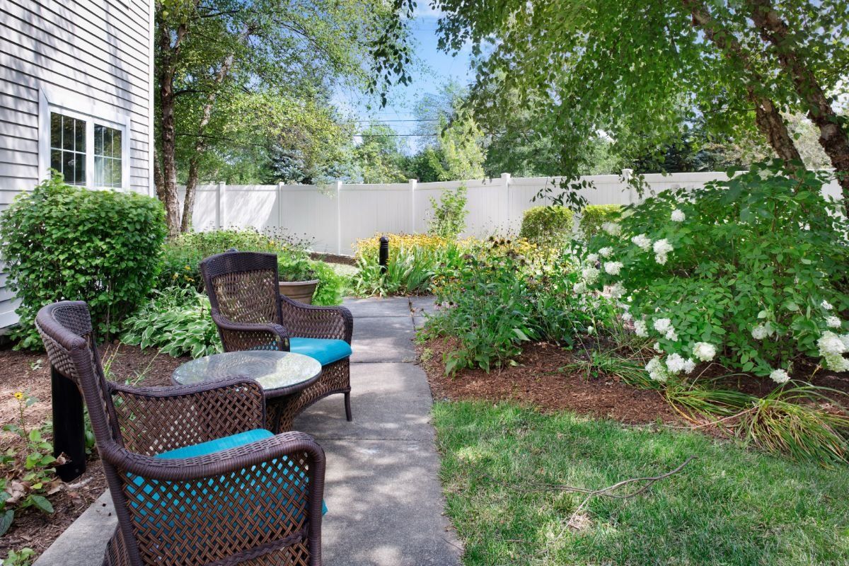 A tranquil garden with a cozy outdoor seating area and a pathway surrounded by lush greenery.