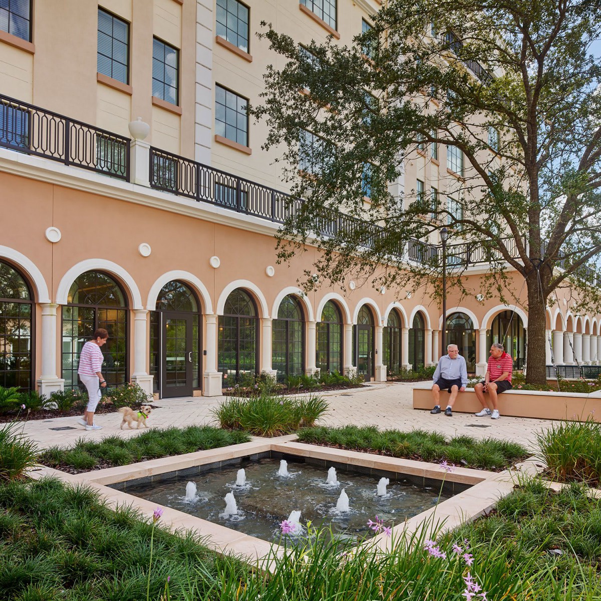 A beautiful courtyard with a fountain surrounded by a landscaped garden and an elegant building.