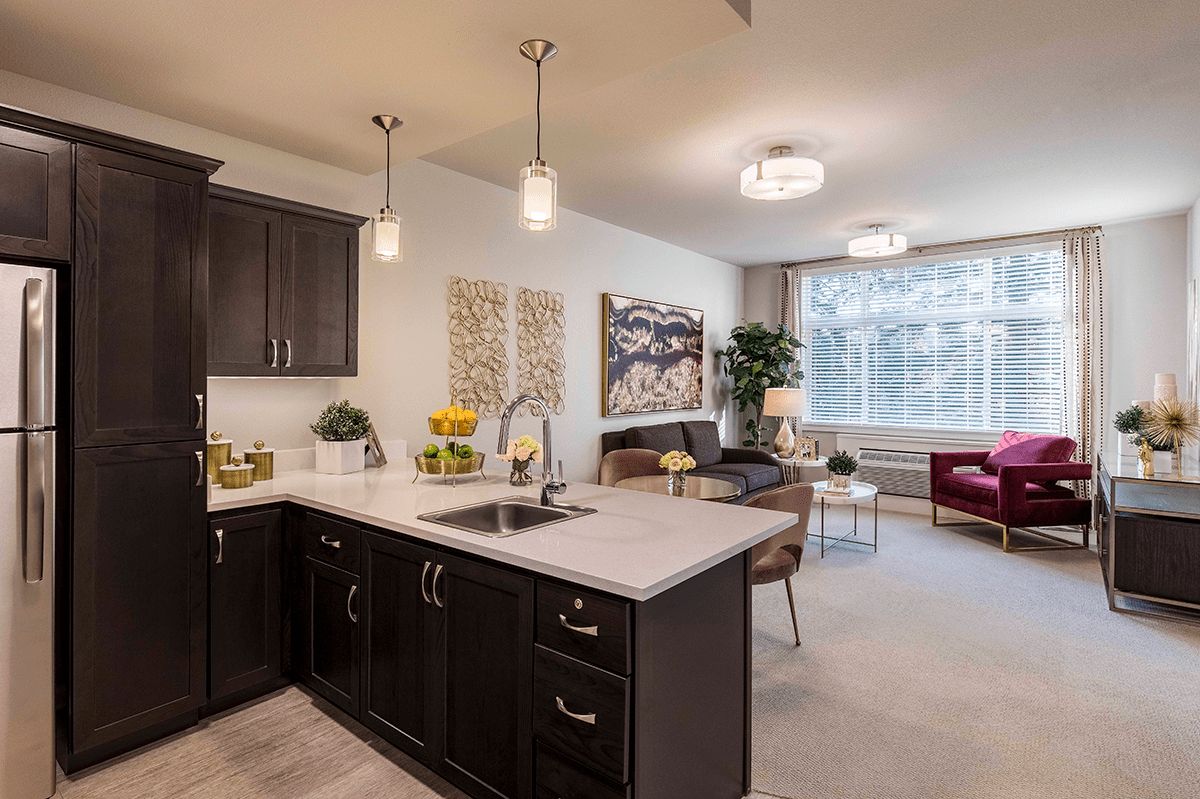 Modern open floor plan kitchen and living room with dark cabinets and stylish lighting.