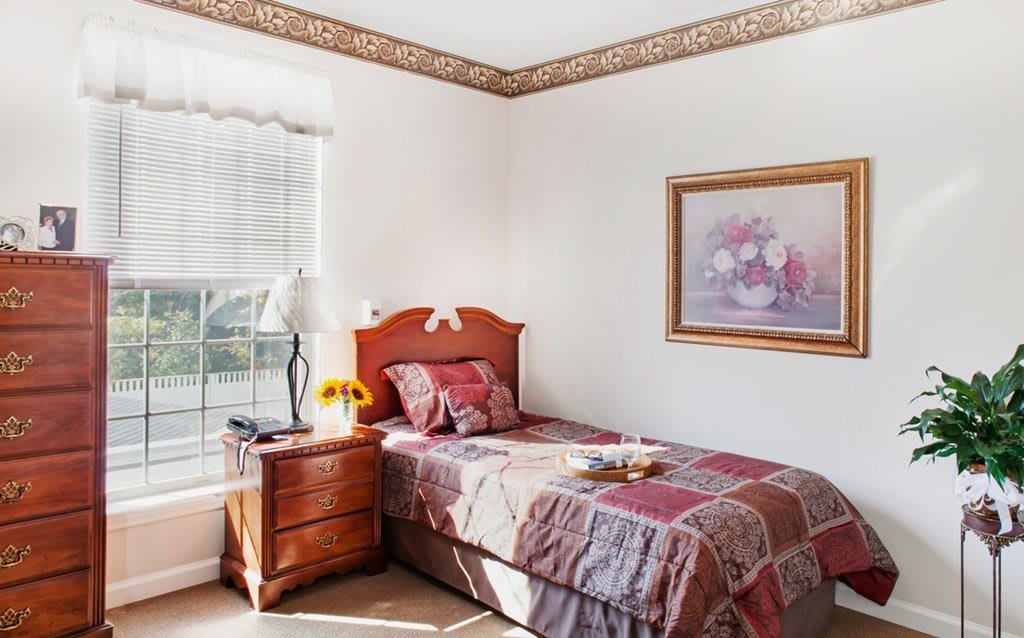 A cozy bedroom with a single bed, adorned with a patterned quilt and lit by natural sunlight streaming through the window.