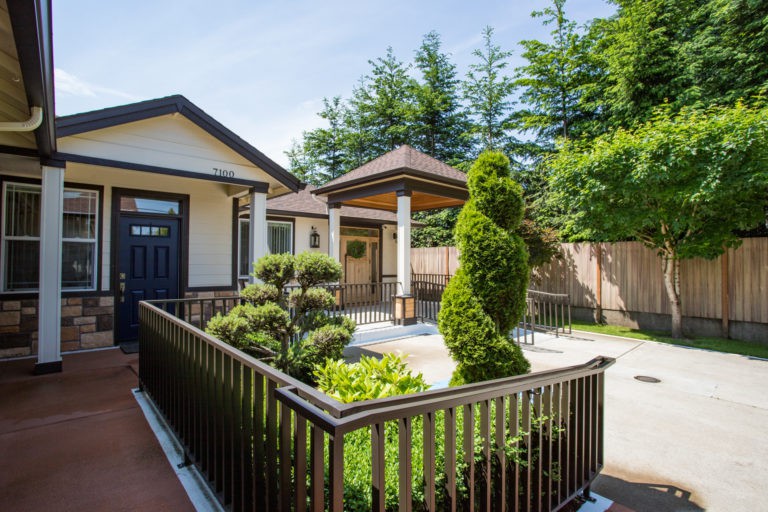A well-maintained garden with topiary and fencing in front of a house entrance.