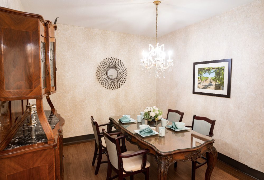 Elegantly set dining room with a classic wooden table and chairs, illuminated by a chandelier.